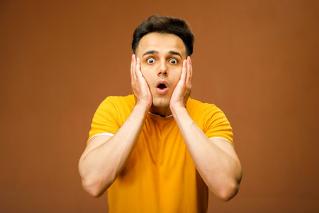 A model is giving a shocking reaction while keeping both hands on his cheek.