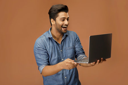 A happy guy is smiling while looking at his laptop.の写真素材