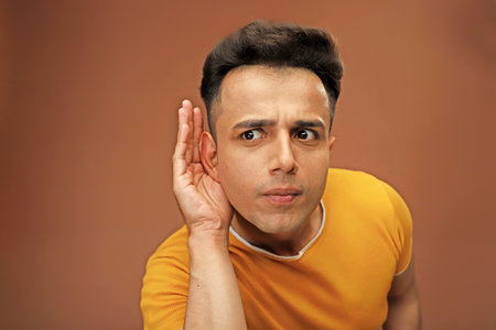 A casual man in casual t-shirt hold his hand on ear trying to listening carefully to the conversation of someone.の写真素材