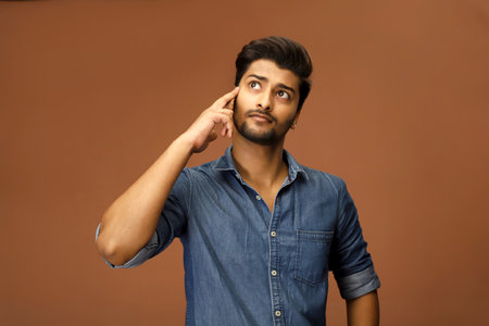 A young male model is thinking something while putting his finger on his head.