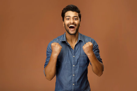 An excited male model celebrates his success by raising his clenched fists.の写真素材