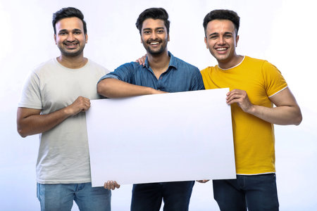 Close-up shot of three happy guys holding a blank white board while posing and smiling.の写真素材