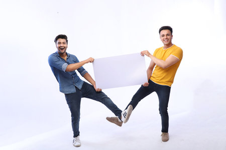 Two friends are holding a white paper board for advertisement and smiling.の写真素材