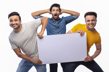 Three friends are posing while standing against a white background and holding a blank white board...