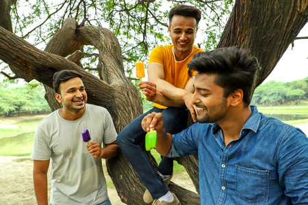 A group of three adult guys are enjoying ice cream in a park and having a good time.の写真素材