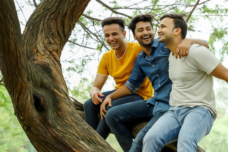 Three friends sitting on tree in park, looking at each other and smilingの写真素材