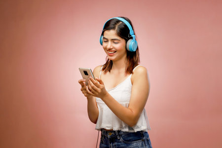Young woman listening to music with headphones and mobile phone on pink backgroundの写真素材