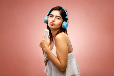 Portrait of a beautiful young woman listening to music with headphones on pink backgroundの写真素材