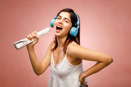 Young woman listening to music with headphones and newspaper on pink background.の写真素材