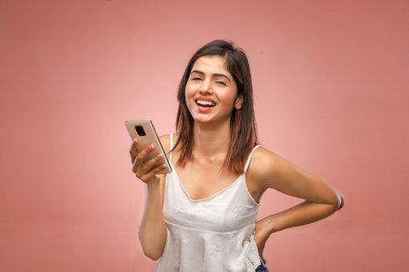 Portrait of a smiling young woman using mobile phone against pink backgroundの写真素材