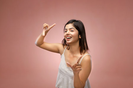 Young asian woman pointing with finger at copy space on pink backgroundの写真素材