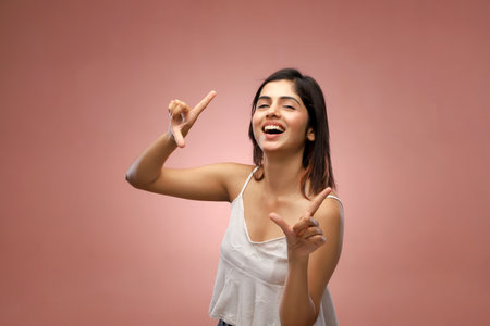 Young woman pointing with her fingers at copyspace on pink backgroundの写真素材