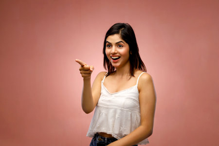 Portrait of a beautiful young woman pointing at something over pink backgroundの写真素材