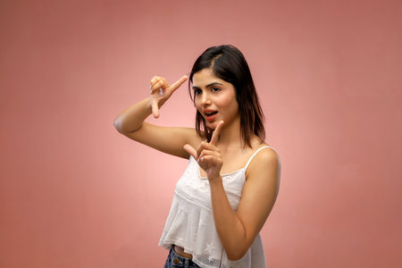 Portrait of beautiful asian woman showing victory sign on pink backgroundの写真素材
