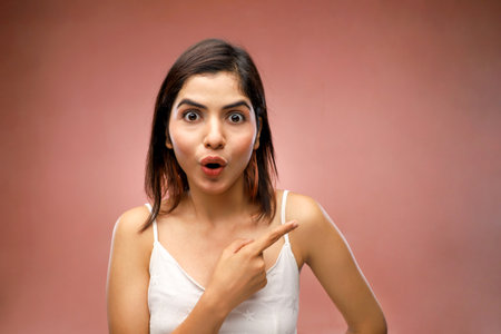 Portrait of a surprised young woman pointing at copy space over pink backgroundの写真素材