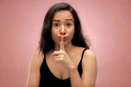 Young woman with finger on lips asking for silence isolated on pink backgroundの写真素材