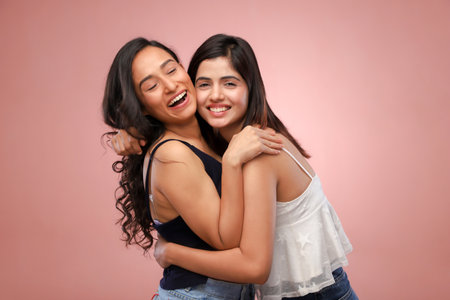 Two asian women embracing each other and looking at camera on pink backgroundの写真素材