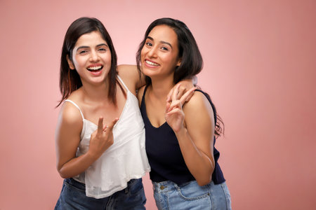 Portrait of two young asian women smiling and having fun isolated over pink backgroundの写真素材