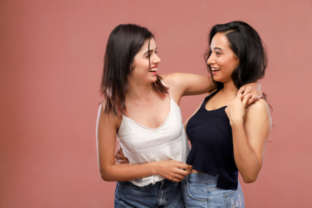 Two young asian women smiling and hugging each other isolated on pink backgroundの写真素材
