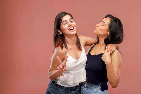 Two young women laughing and having fun together on a pink background.の写真素材