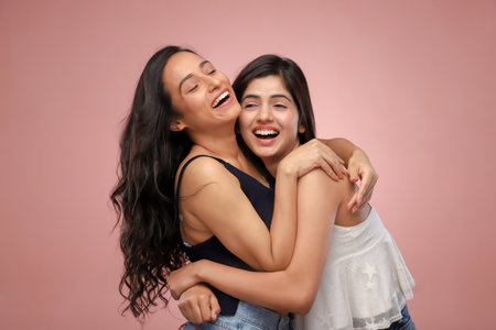 Two young Asian women laughing and hugging each other on pink background.の写真素材
