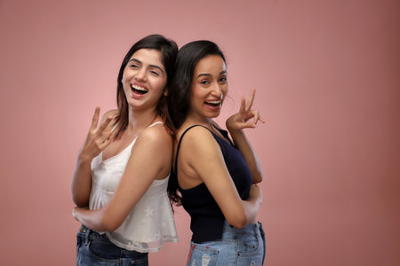 Two beautiful asian women in jeans and t-shirts posing against pink backgroundの写真素材