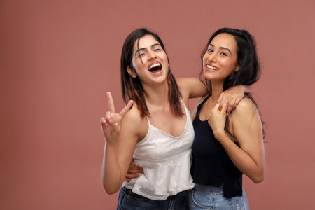 Portrait of two young women having fun together. Isolated on brown backgroundの写真素材