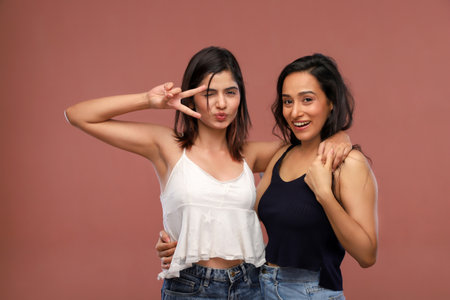 Portrait of two asian women showing peace sign isolated on brown backgroundの写真素材