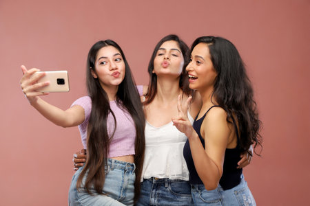 Three young asian women taking selfie with mobile phone on pink backgroundの写真素材