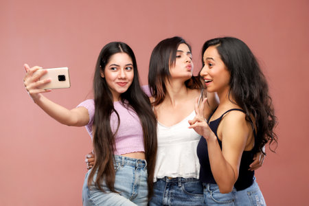 Three young asian women taking selfie with mobile phone on pink backgroundの写真素材