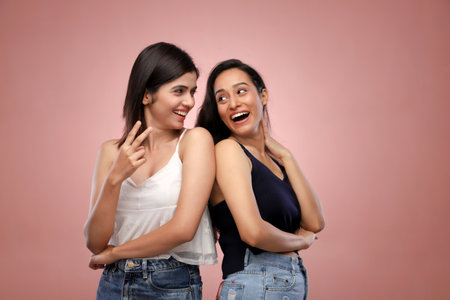 Two young asian women in jeans and black top on pink backgroundの写真素材