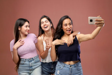 Group of young women taking a selfie with a mobile phone on a pink backgroundの写真素材