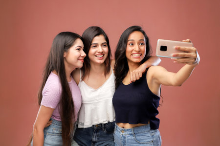 Group of young women taking a selfie with a mobile phone isolated on a pink backgroundの写真素材