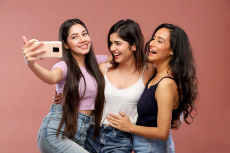 Group of young women taking selfie with mobile phone. Isolated on pink background.の写真素材