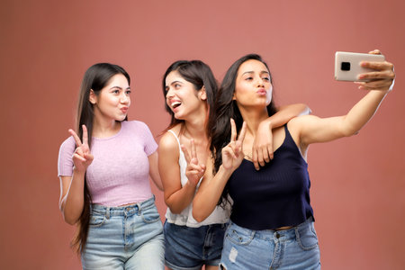 Group of happy young women taking selfie with mobile phone isolated on brown backgroundの写真素材