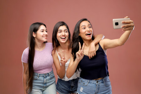 Group of three happy young women taking selfie with mobile phone isolated over pink backgroundの写真素材