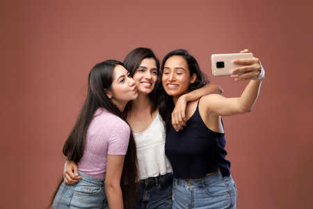 Three young asian women taking selfie with mobile phone on pink backgroundの写真素材