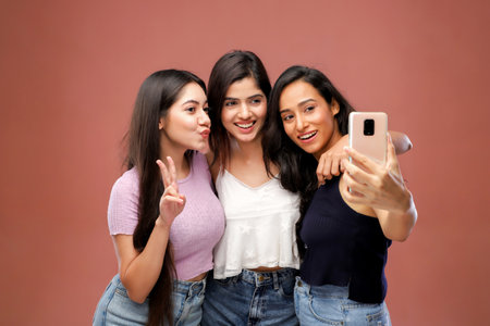 Three asian women taking selfie with mobile phone on brown background.の写真素材
