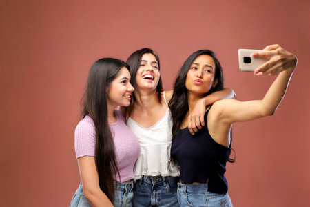Group of young women taking a selfie with a mobile phone on a pink backgroundの写真素材
