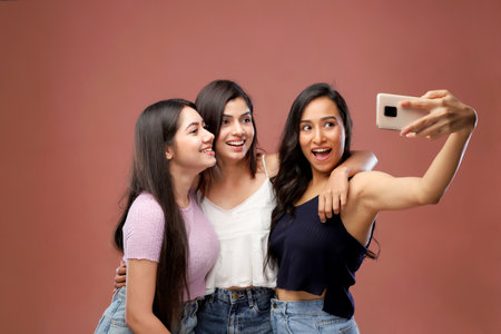 Three young asian women taking selfie with mobile phone on pink backgroundの写真素材