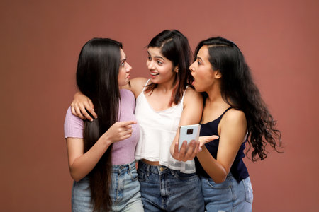 Three young asian women taking selfie with mobile phone isolated on brown backgroundの写真素材