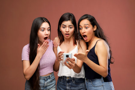 Three young asian women looking at mobile phone with surprised face.の写真素材