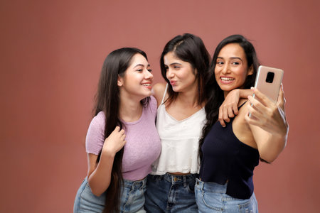 Group of young women taking a selfie with mobile phone isolated on brown backgroundの写真素材
