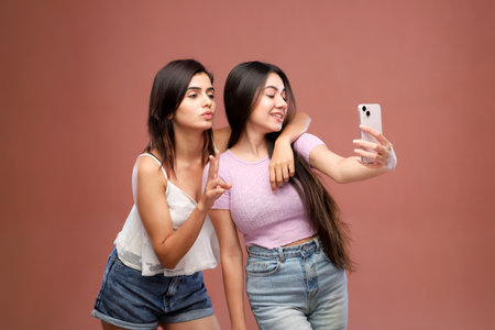 Portrait of two young women taking selfie with mobile phone on brown backgroundの写真素材