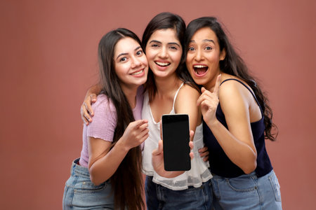 Portrait of three happy teenage girls showing smartphone with blank screen and smilingの写真素材