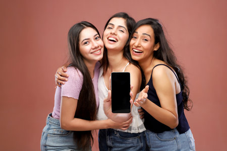 Three young asian women holding smart phone with blank screen over pink backgroundの写真素材