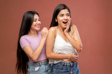Two young women laughing and looking at each other on a brown backgroundの写真素材