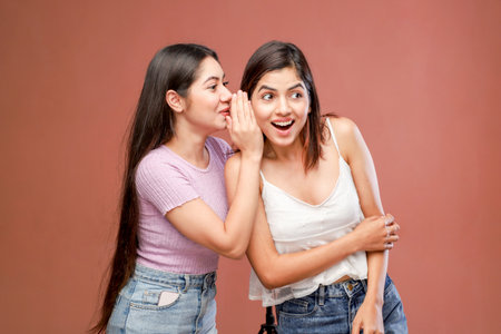 Portrait of two young women gossiping and gossiping on brown backgroundの写真素材