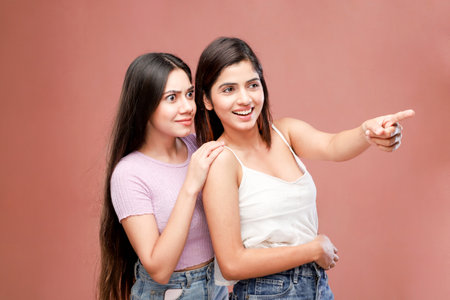Two beautiful young women pointing at something on a pink background with copy spaceの写真素材
