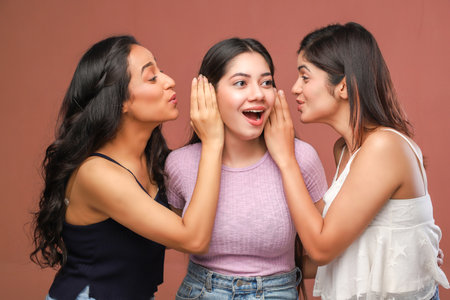 Three young asian women whispering gossip to each other on brown backgroundの写真素材